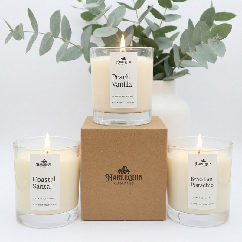 A collection of three Harlequin Candles in clear glass jars featuring Avocado Mint, Kakadu Plum, and Peach Vanilla scents.