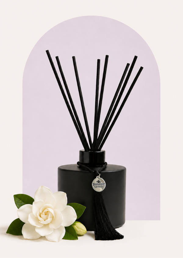 An Australian made Harlequin Candles reed diffuser featuring gardenia and lilac fragrance, perfect for a long-lasting floral home scent. The bottle is set against a purple background with white gardenia flowers.