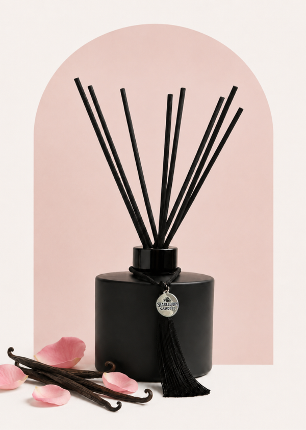 An Australian made Harlequin Candles black matte reed diffuser featuring a delicate floral home fragrance of marshmallow, musk, rose placed on a pink background.