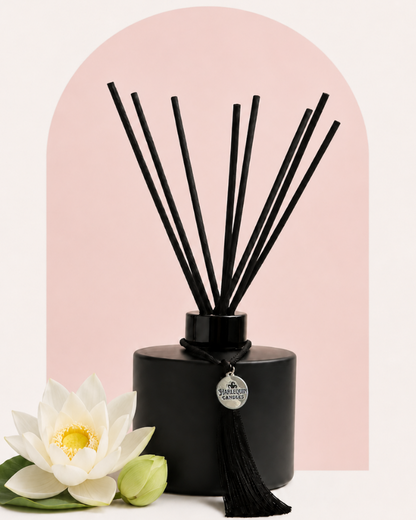 An Australian made Harlequin Candles black matte reed diffuser featuring a delicate floral home fragrance of white lotus, placed on a pink background with jasmine flowers.