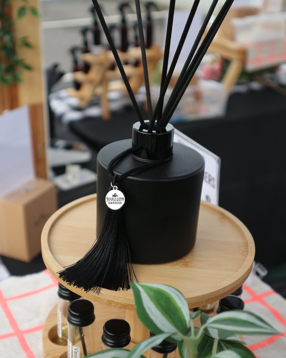 Black Harlequin Candles reed diffuser with fibre reeds and tassel displayed with fragrance testers at Bentleigh Sunday Market in Melbourne.