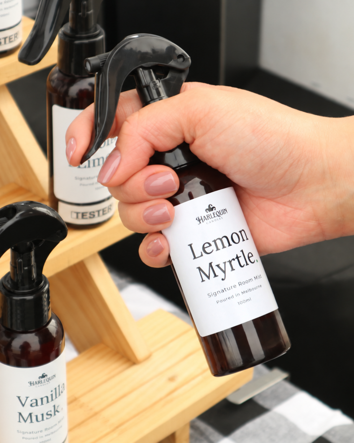 Lemon Myrtle room mist by Harlequin Candles being held at a Melbourne market stall, with other handmade room mists displayed in the background.