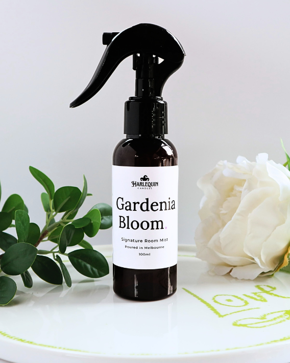 Luxury Gardenia Bloom home fragrance spray styled with fresh green leaves and white gardenia flowers on a designer ceramic tray, sophisticated floral room deodorizer by Harlequin Candles.