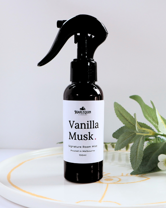 Luxury Vanilla Musk home fragrance spray styled with green botanical leaves on a white designer tray, sophisticated room deodorizer and aromatherapy mist by Harlequin Candles.